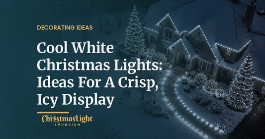 Aerial view at night of a snowy stone house with its gables and roofline outlined in cool white C9 bulbs, two tall spruces wrapped in cool white mini lights, shrubs covered in cool white net lights, and a curving walkway lined with cool white bulbs