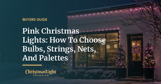 A white brick corner cafe on a snowy night with its roofline and front window outlined in pink C9 Christmas bulbs and two potted evergreens wrapped in pink and white mini lights