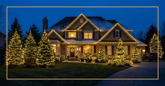 Suburban two-story home at twilight with warm white LED Christmas lights glowing on the roofline and wrapped around evergreen trees and bushes in the front yard, deep blue dusk sky