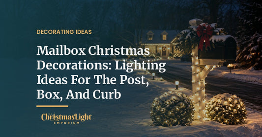 A black mailbox at the end of a snowy driveway at night, its post spiral-wrapped in warm white mini lights, two round shrubs in warm white net lights, and low path lights leading to a lit house