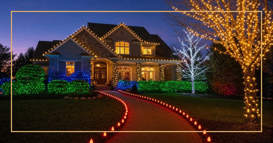 Upscale suburban home at twilight showcasing multiple Christmas light colors — warm white on roofline, red C9 bulbs along walkway, blue and green LEDs in hedges, golden amber on trees