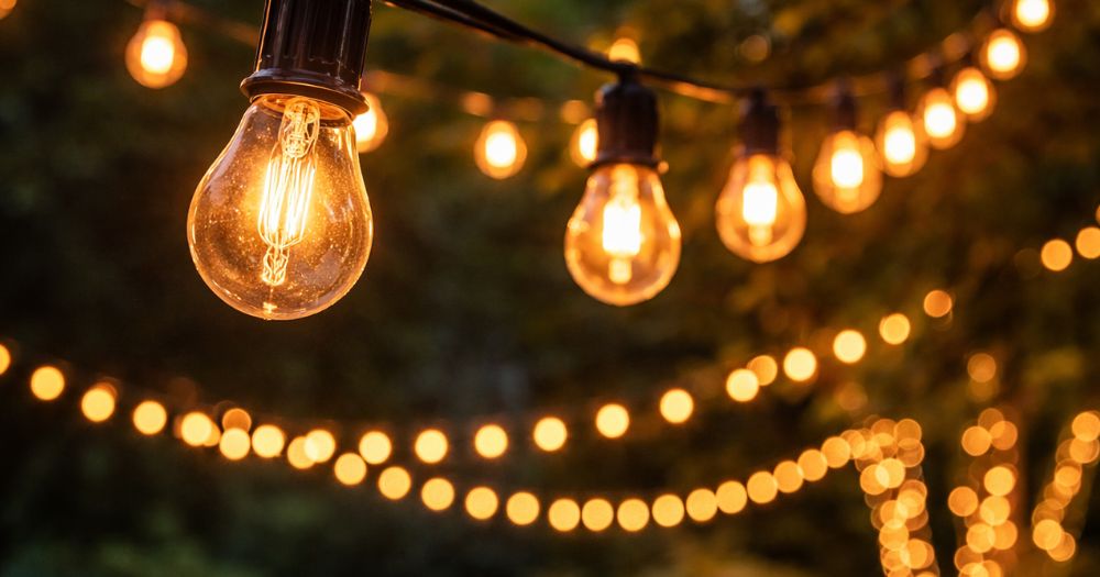 Warm vintage Edison bulb string lights draped overhead in evening darkness, creating cozy outdoor ambiance for spring patios.