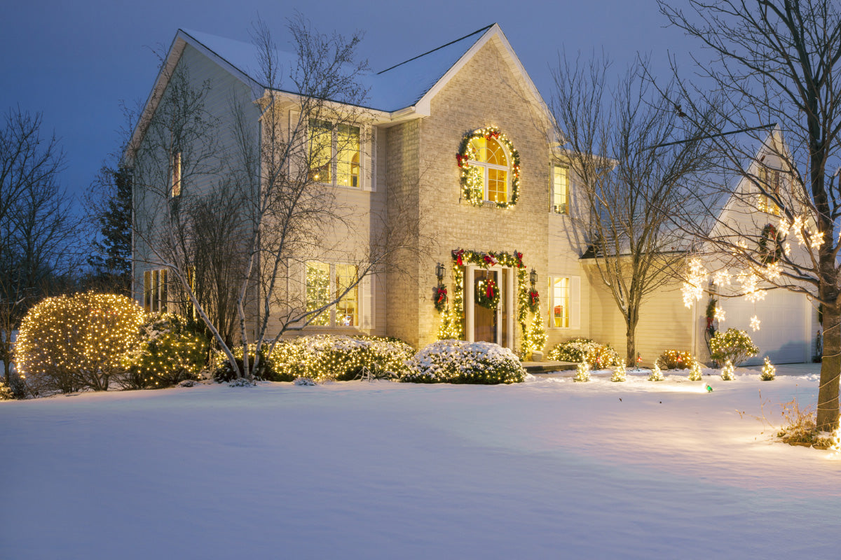 Two story house decorated with warm Christmas lights on the roofline, windows and landscaping