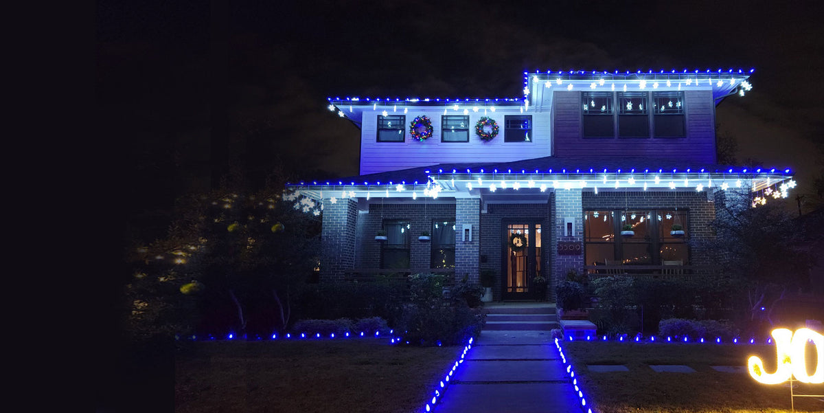Suburban home at dusk with warm white Christmas lights along the roofline and landscaping