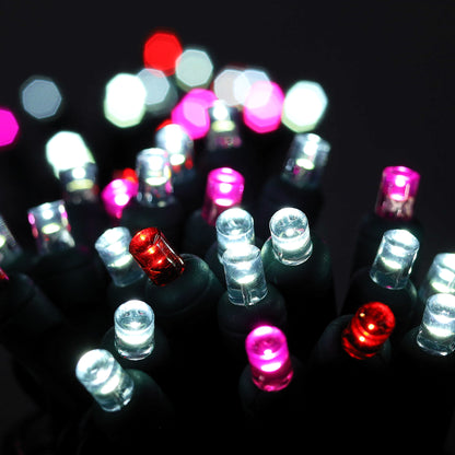 Close-up of lit ColorCraft® Cupid 5mm LED Christmas lights glowing cool white, red, and pink on green wire