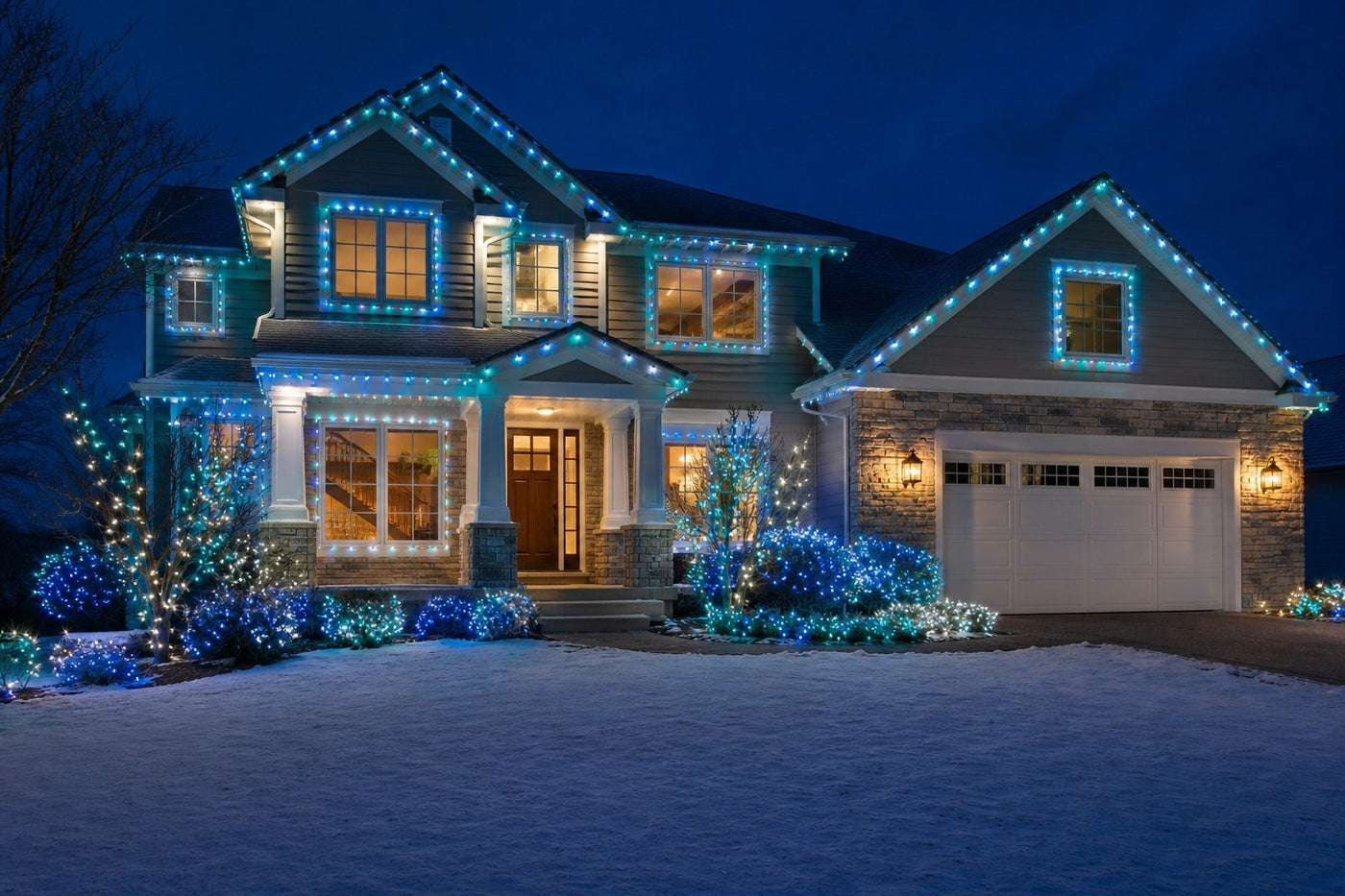 Two story house at night decorated with ColorSplash Arctic style teal, blue and cool white mini LED Christmas lights on the roofline, windows and shrubs