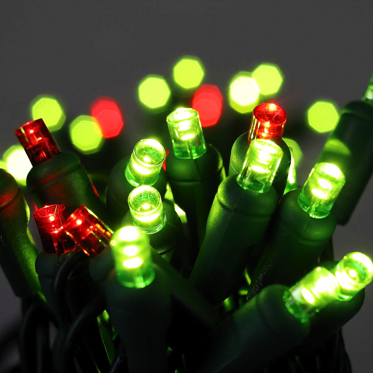 Close-up of lit ColorCraft® Humbug 5mm LED Christmas lights glowing lime green and red on green wire