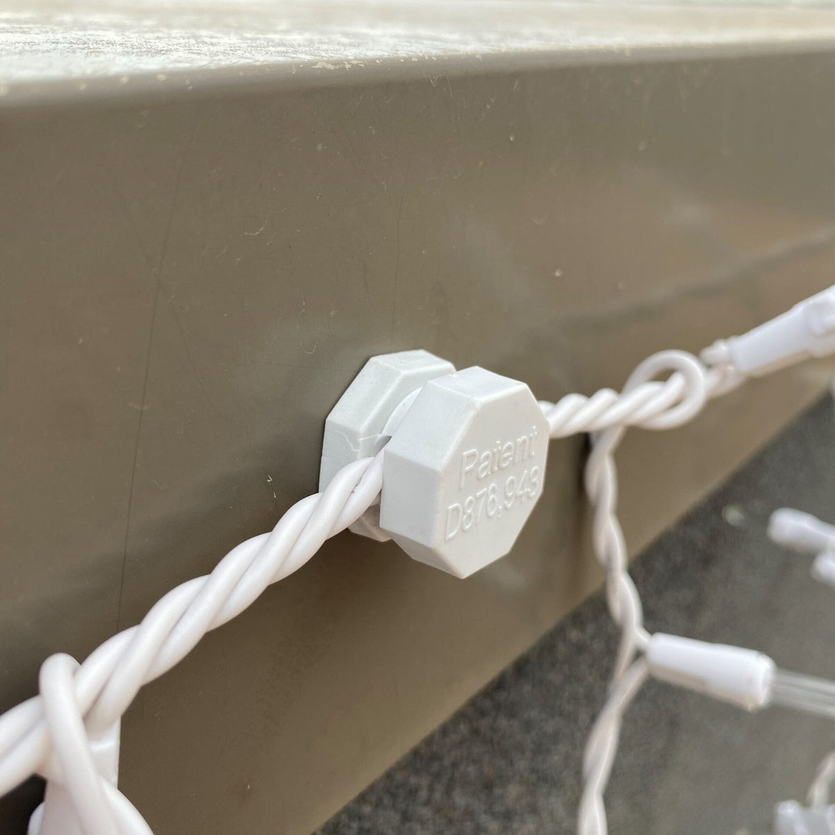 White Lite-Netics magnetic wire clamp holding icicle light wire against a tan metal fascia