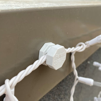 White Lite-Netics magnetic wire clamp holding icicle light wire against a tan metal fascia