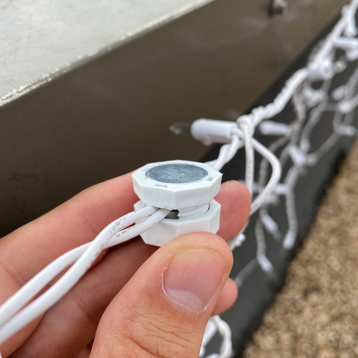 Hand attaching a white Lite-Netics magnetic wire clamp to icicle light wire on a metal edge