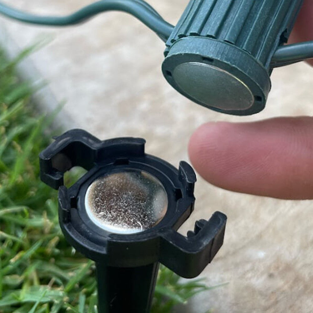 Hand placing a magnetic C9 socket onto a Lite-Netics metal base lawn stake in grass