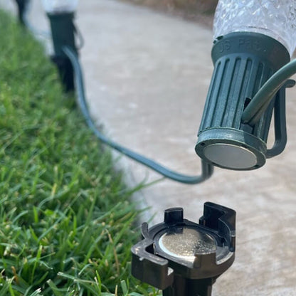 Lite-Netics magnetic C9 socket snapped onto the metal base of a black lawn stake in grass