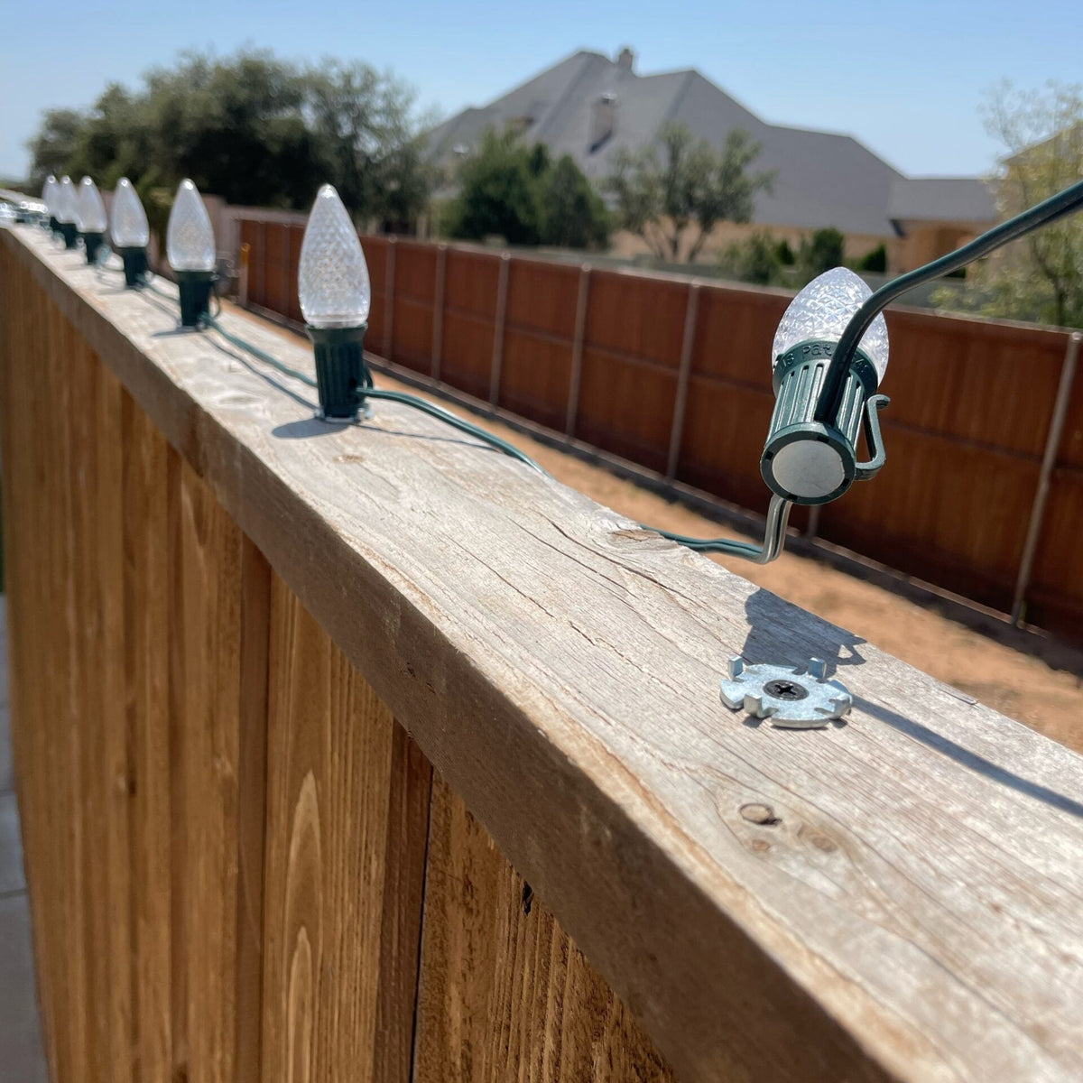 Close-up of Lite-Netics magnetic C9 sockets on nickel clips screwed to a wood fence