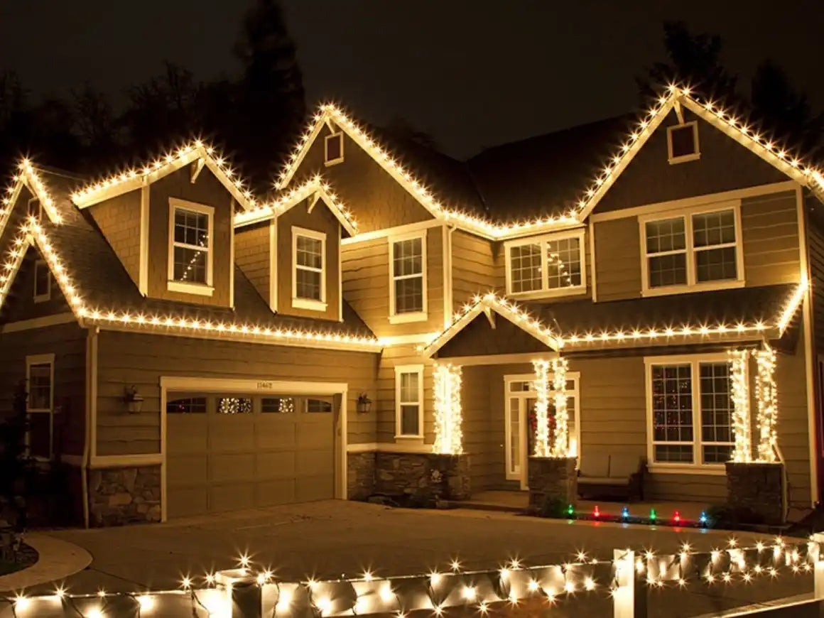 A two-story house with warm white Christmas lights outlining its rooflines and porch columns.